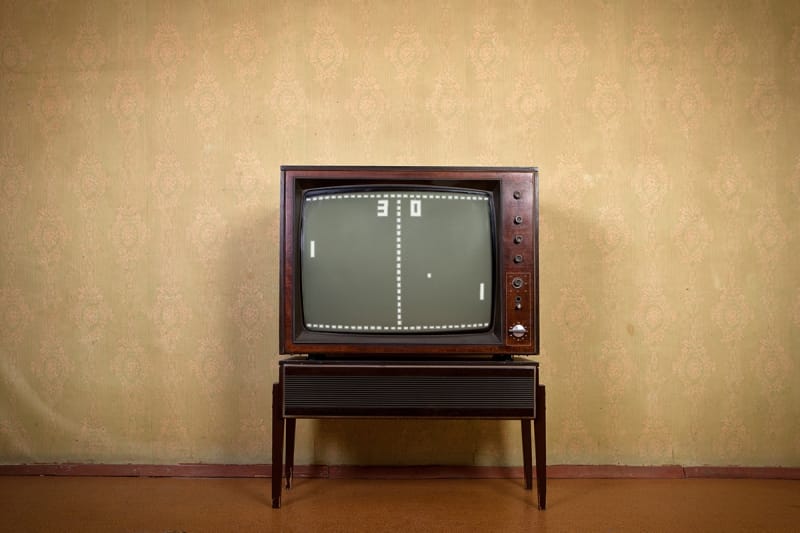 A retro style television, displaying a black and white game of Pong being played